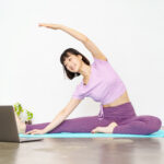 パソコンを開きながらヨガをする女性の写真